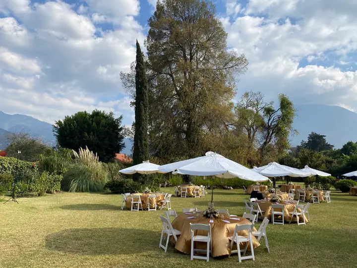 A garden with round tables and white umbrellas, with the mountains in the background